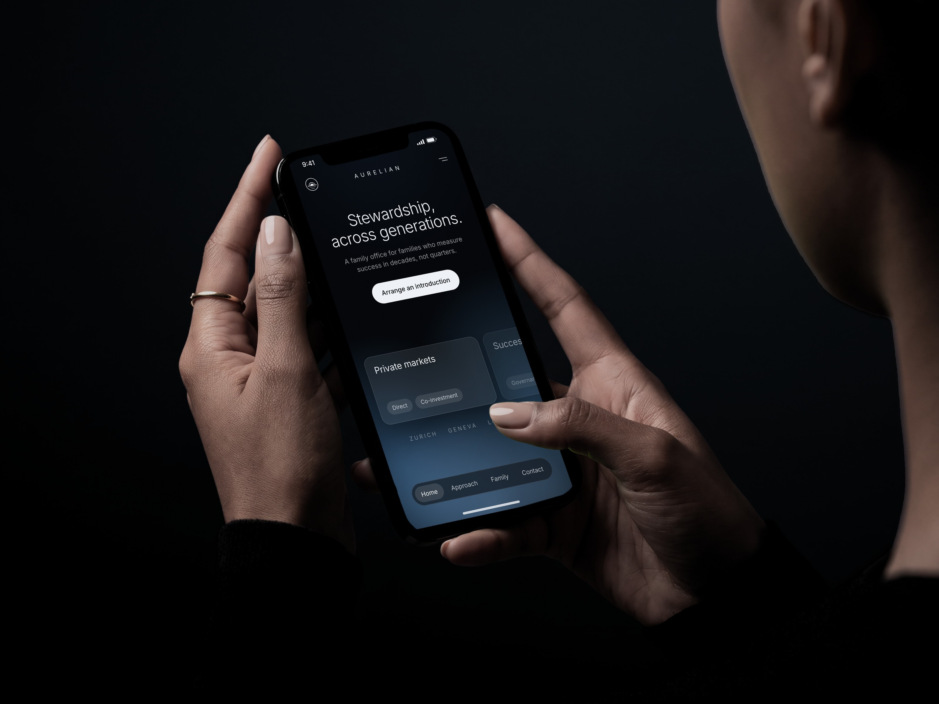 A woman's hands hold a phone showing a family office's site, “Stewardship, across generations”, against deep navy falling to black